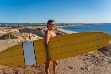 Çekici Avustralyalı olgun sörfçü günbatımında kaliteli sörf tahtasıyla. 50 'li yaşlardaki zinde kadın sörf yapmaya döndüğü için mutlu. Açık hava sporları, aktif yaşlılar ve emeklilik hayatı..