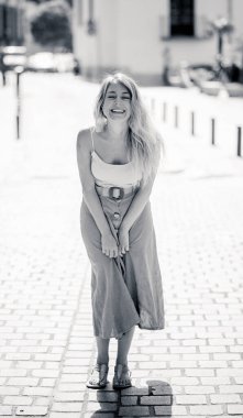 Açık havada, güzel sarı saçları ve şehvetli gülüşü olan çekici bir kadının uzun boylu portresi. Doğal güzellik ve ışıkla poz veren kadın model. Gerçek insanlar, güzellik, moda ve yaşam tarzı.