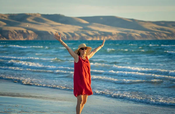快乐迷人的成熟女人 穿着红色衣服 在户外尽情享受 在海滩上自由自在 张开双臂 伸展着蓝色的大海和美丽的风景 退休生活方式和福利概念 — 图库照片