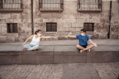 Korumacı yüz maskeleri takan erkek ve kadın birbirlerinden 2 metre uzakta duruyorlar. Sosyal mesafeyi koronavirüsün yayılmasını önlüyorlar. COVID-19 hastalıkların korunmasının kavramsal görüntüsü ve Yeni Normal.