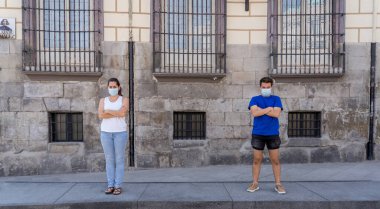 Korumacı yüz maskeleri takan erkek ve kadın birbirlerinden 2 metre uzakta duruyorlar. Sosyal mesafeyi koronavirüsün yayılmasını önlüyorlar. COVID-19 hastalıkların korunmasının kavramsal görüntüsü ve Yeni Normal.