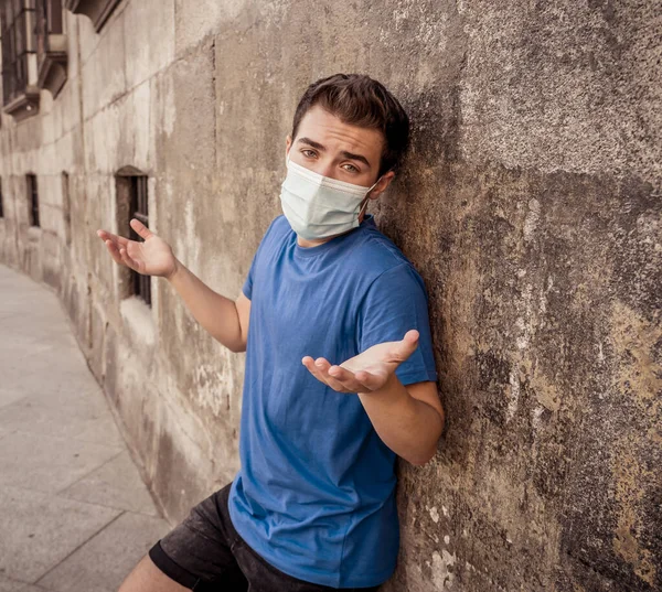 Young sad desperate man wearing surgical face mask in public spaces. Man with protective mask walking outdoors city street after coronavirus outbreak lockdown. New Normal life and COVID-19.