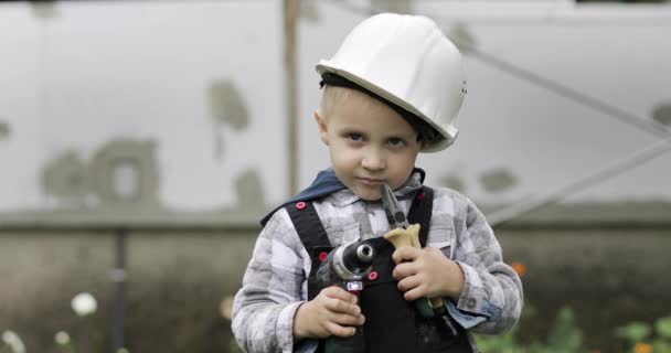 Retrato de um pequeno construtor em um capacete branco com uma chave de fenda e alicate. — Vídeo de Stock