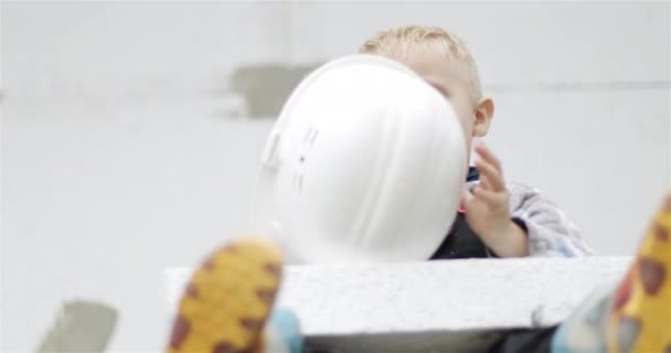 Menino colocando em um capacete construtor branco. — Vídeo de Stock