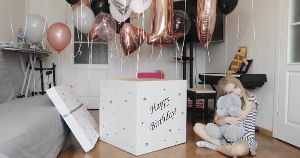 Gelukkig meisje knuffels een zacht speelgoed beer op de achtergrond van ballonnen en geschenken. — Stockvideo