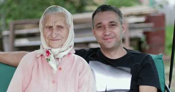 Eine ältere Frau mit tiefen Falten sitzt zusammen mit einem jungen Mann auf einer Schaukel . — Stockvideo