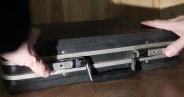 Erkek eller eski siyah bir bavulu açar.. 