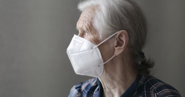 Tıbbi maskeli yaşlı kadın pencereden dışarı bakıyor.. — Stok video