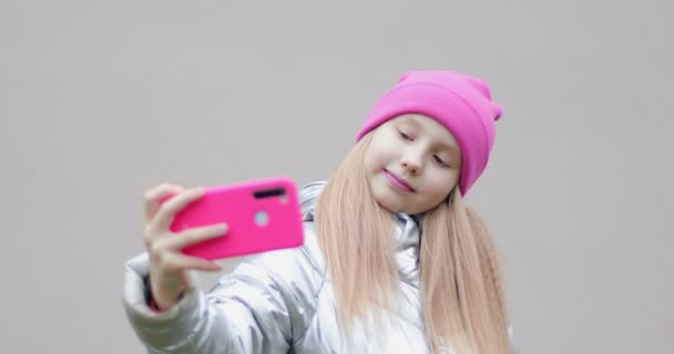 En modern skolflicka i rosa hatt gör en selfie utomhus. — Stockvideo