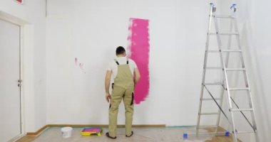 Boyacı evin duvarını boyuyor, boya rulosu ve pembe boyayla..