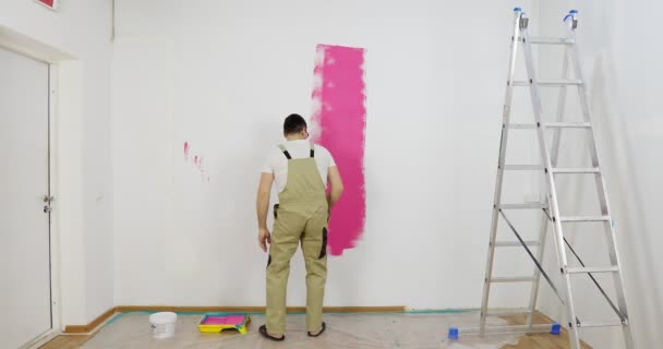 Ζωγράφος άνθρωπος ζωγραφική στον τοίχο στο σπίτι, με ρολό χρώμα και ροζ χρώμα χρώμα. — Αρχείο Βίντεο