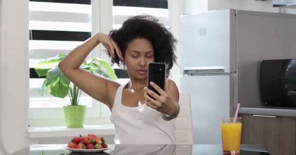 En modern afroamerikansk modell tar en selfie på sin telefon i köket. — Stockvideo