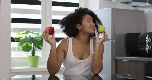 Una mujer negra está sentada en la cocina y comiendo fruta. — Vídeos de Stock