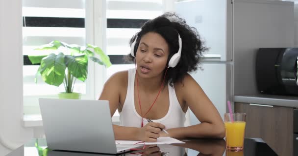 Afro amerykańska kobieta w słuchawkach studiuje online z domu oglądając internet. — Wideo stockowe