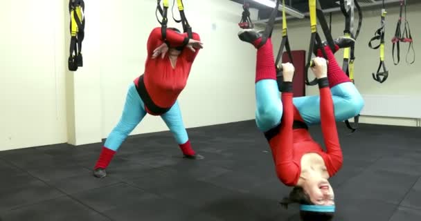 Fat and thin women in red leggings hang from sports ropes. — ストック動画