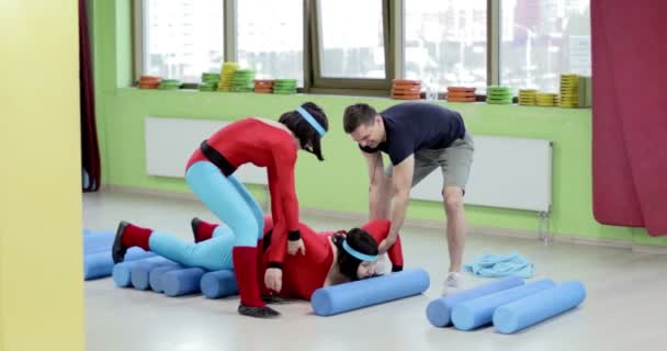 Een trainer en een jong meisje tillen een dikke vrouw in een rood pak van de vloer. — Stockvideo