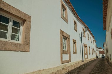 Facade of old whitewashed houses and cute windows in cobblestone alley, on a sunny day at Marvao. An amazing medieval fortified village in Portugal.