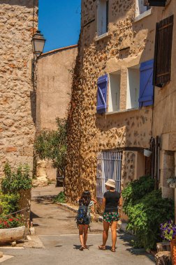 Chateaudouble, Fransa - 11 Temmuz 2016. Ortaçağ kökenli bir köy olan Chateaudouble 'da güneşli bir günde sokakta bina ve çiçeklerle yürüyen kadın ve çocuk. Provence bölgesi, Fransa.