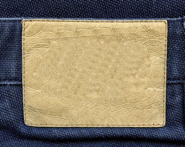 Beige old  blank leather label on background of blue fabric — Stock Photo, Image