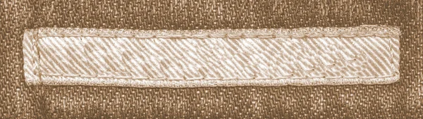 Etiqueta têxtil marrom pálido no fundo jeans marrom — Fotografia de Stock