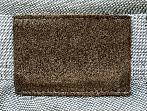 Brown leather label on gray jeans background — Stock Photo, Image