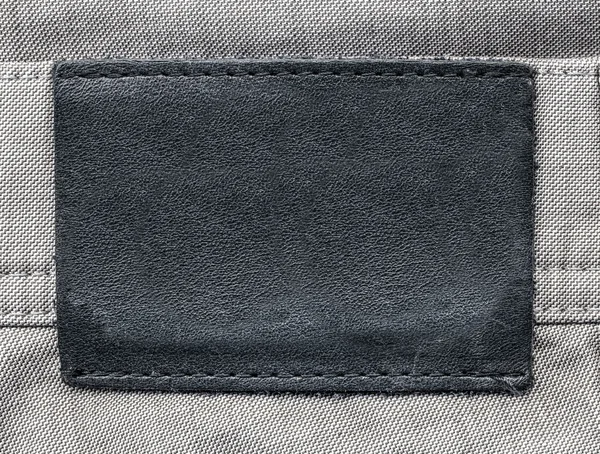 Etiqueta de couro marrom escuro em branco no fundo de jeans cinza — Fotografia de Stock