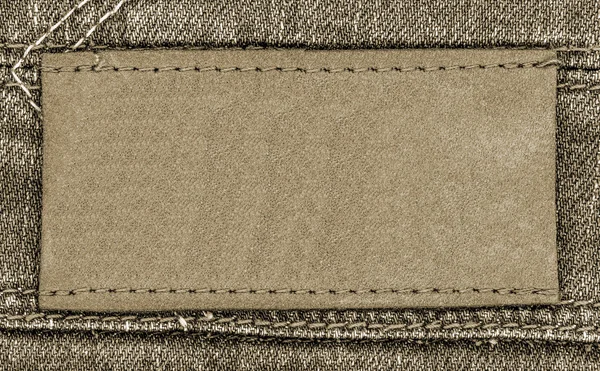 米色的空白皮革标签上棕色的牛仔裤背景 — 图库照片