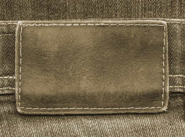 Hnědá kožená štítek na pozadí hnědé džíny — Stock fotografie