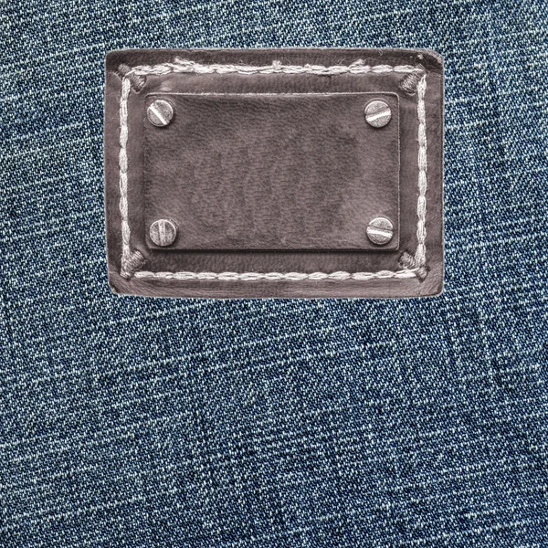 Textura azul denim, etiqueta de couro marrom em branco — Fotografia de Stock