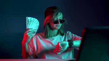 Gözlüklü hacker kız dizüstü bilgisayarda oturuyor ve para fanı sallıyor.
