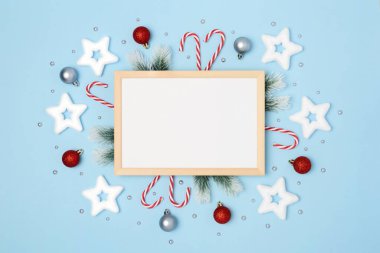 Tahta çerçeve, yazı için beyaz yer. Yılbaşı dalları, ağaç süslemeleri ve noel şeker kamışlarıyla. Açık mavi arka planda yıldızlar ve noel baloları. Flatlay. Uzayı kopyala Kimse..