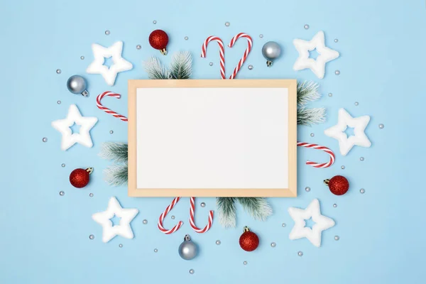 Tahta çerçeve, yazı için beyaz yer. Yılbaşı dalları, ağaç süslemeleri ve noel şeker kamışlarıyla. Açık mavi arka planda yıldızlar ve noel baloları. Flatlay. Uzayı kopyala Kimse..