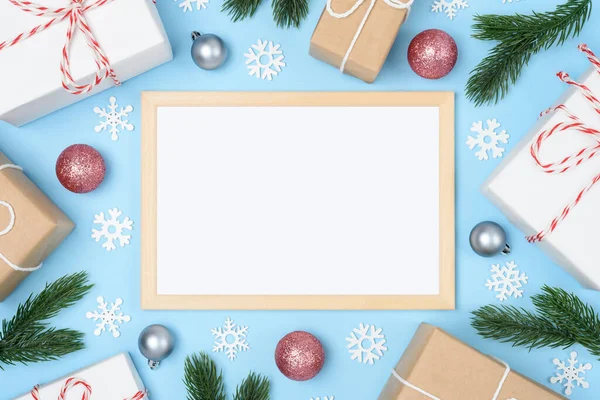 Tahta çerçeve, yazı için beyaz yer. Noel ağacı süslemeleri ve kar taneleriyle yılbaşı dalları. Açık mavi arka planda Xmas hediyeleri. Flatlay. Uzayı kopyala Kimse..