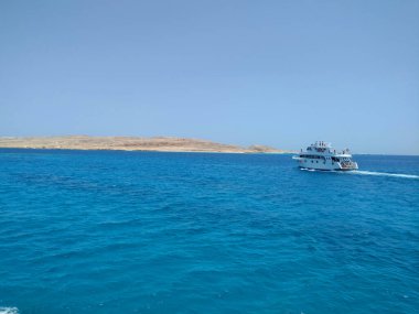 Tropikal denizde lüks bir özel motor yatı sürüyor. Adanın etrafında gökyüzünün arka planında bulutlarla.