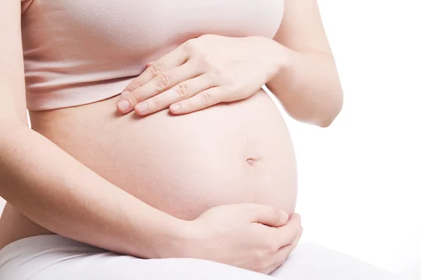 Mulher grávida com as mãos sobre a barriga no fundo branco — Fotografia de Stock