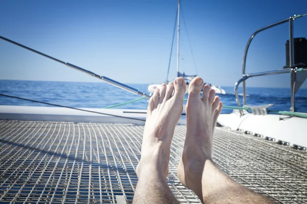 Man lounging on a catamaran sailboat trampoline with her feet propped up and crossed. — Stock Photo, Image
