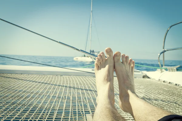 Man lounging on a catamaran sailboat trampoline with her feet propped up and crossed. — Stock Photo, Image