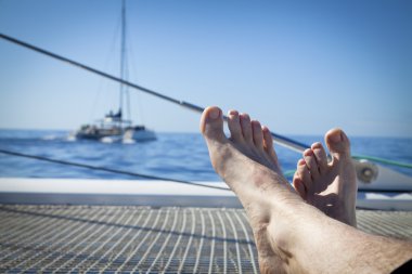 Ayaklarını propped ve çarpı işareti ile bir katamaran yelkenli trambolin üzerinde uzanmanız adam.