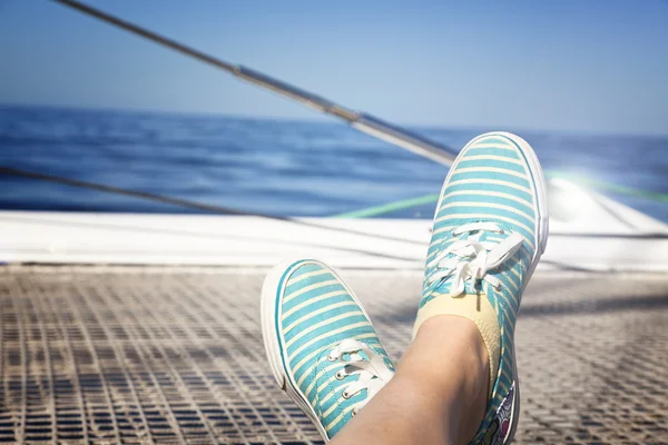 Woman relaxing on a catamaran sailboat trampoline with her feet crossed — Stock Photo, Image