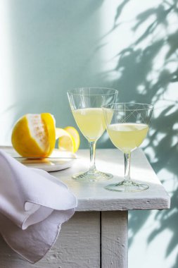 Kristal bardaklarda İtalyan limonçellosu ve ahşap bir masada olgun limonlar..