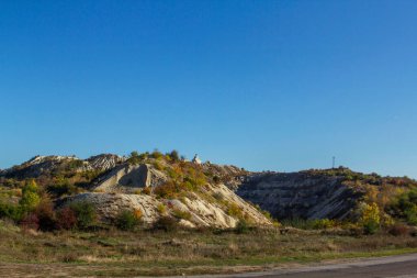 Kuzey Moldova 'da ormanlık ve dağlık arazi boyunca uzanan bir sonbahar manzarası. Kireçtaşı ocaklarında çalılıklar var. Güneşli manzara.