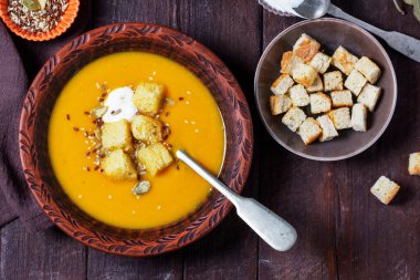 Kabak kremalı çorba, kızarmış ekmek, krema ve tohumla servis edilir. Koyu bir ahşap masada sonbahar sebze çorbası. Kırsal biçim, seçici odak.