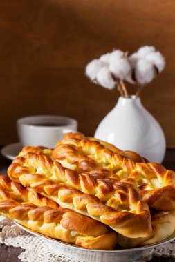 Süzme peynirli çörekler, çay ile servis edilir. Maya esaslı hamur işleri, bir fincan siyah çay ve ahşap bir masada pamuk çiçekleri. Kırsal biçim.