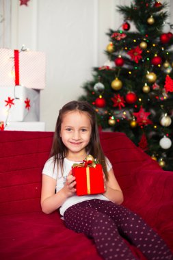 Kırmızı bir kutu, Hediyelik, yılbaşı ağacı arka planda tutan kanepede oturan küçük kız