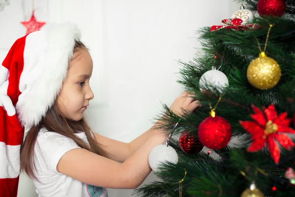 Menina em boné vermelho pendura na árvore de Natal novos brinquedos ano — Fotografia de Stock