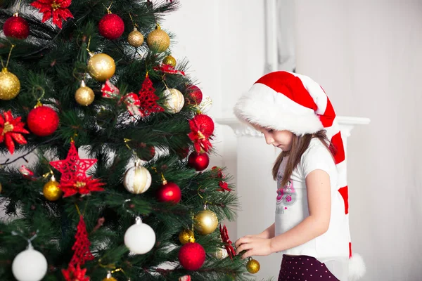 Little girl in  red cap hangs on the Christmas tree new year toys — Stock Photo, Image