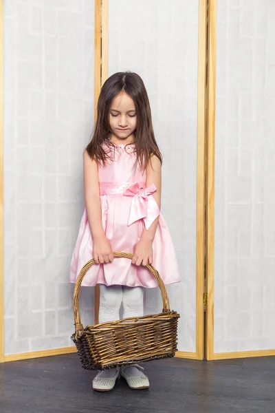 Little girl in a pink dress with white shoes holding brown basket — Stock Photo, Image