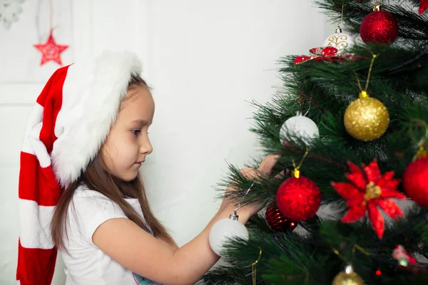 Little girl in  red cap hangs on the Christmas tree new year toys Stock Image