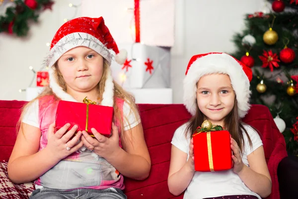 Duas meninas trajes de Natal sentado no sofá com presentes na mão, fundo da árvore — Fotografia de Stock