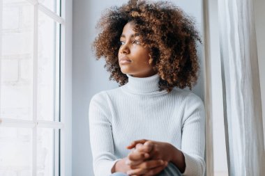 Modern beyaz pencere eşiğinde oturan düşünceli genç kadın.